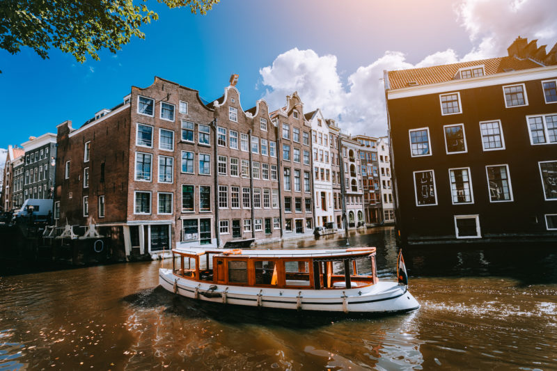 City of Amsterdam in Holland picturesque scenery, white boats on a canal between historic houses.